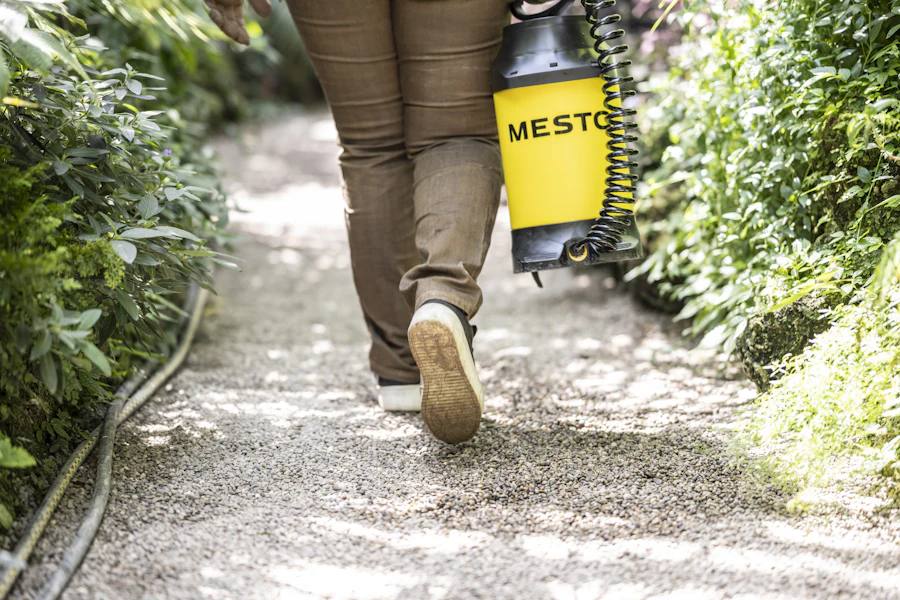 Person walking a yard path carrying a backpack sprayer